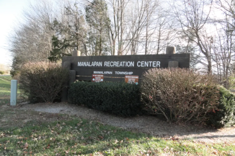 Sign for Manalapan Recreation Center surrounded by bushes and bare trees.