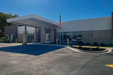 Modern building with a flag, large windows, and a spacious parking lot.