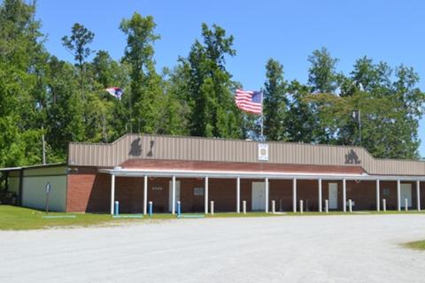 Large building with brown roof, two flags, and trees in background.