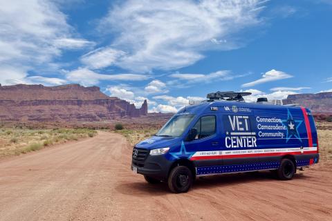 Blue "VET Center" van on dirt road with desert hills in background.
