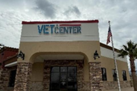 Vet Center building with flag, cloudy sky, and palm trees.