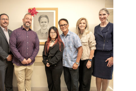 Group of people stand in front of framed photo of a man.