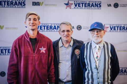 Three men standing together in front of a Veterans backdrop.