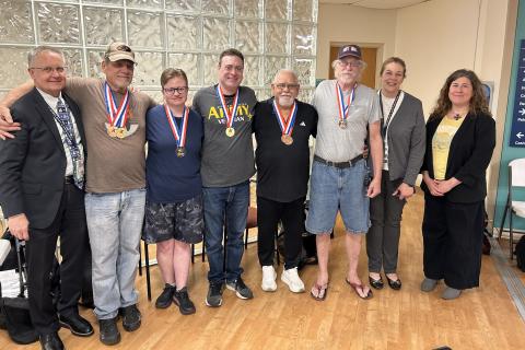 Seven adults, wearing medals, pose for a photo in a room.