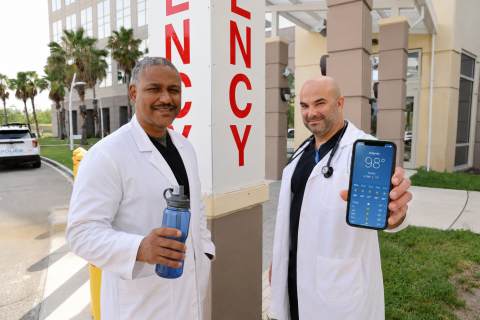 Two doctors in white coats holding a smartphone outside a hospital.