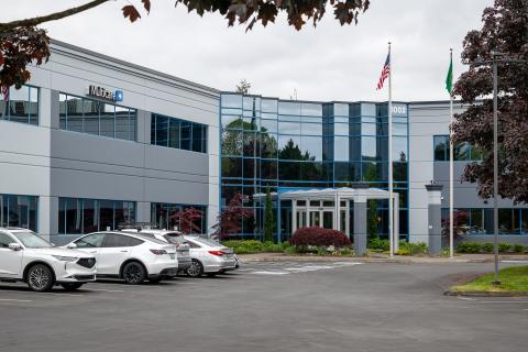 Modern office building with parked cars, flags, and surrounding greenery.