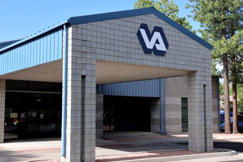 Blue and white building entrance with "VA" logo, surrounded by trees and a clear sky.
