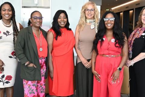 Seven women in elegant dresses posing for a photo.
