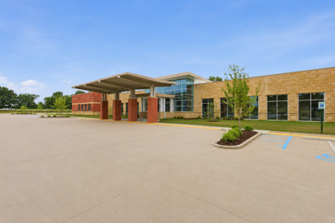 Large, modern building with a covered entrance and a spacious parking lot.