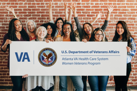 Group of women veterans holding a sign in front of brick wall.