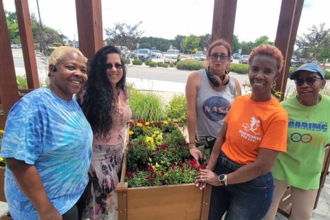 Five women stand together in front of a flower planter.