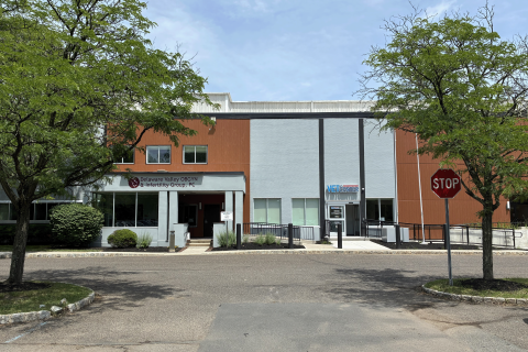 Exterior of building with orange and gray panels, trees, and stop sign.