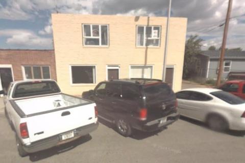 White pickup truck, black SUV, and white sedan parked in front of a yellow building.
