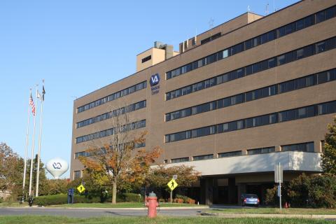 Brown, multi-story building with many windows, surrounded by trees and grass.