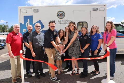 Group of people cutting a ribbon in front of a white ambulance.
