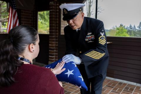 A sailor in uniform presenting a folded flag to a woman.