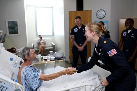 A military servicewoman shakes hands with a patient in a hospital bed.