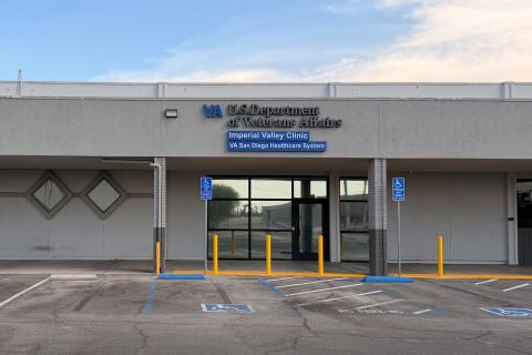 Exterior of building with parking lot, blue signs, and yellow bollards.