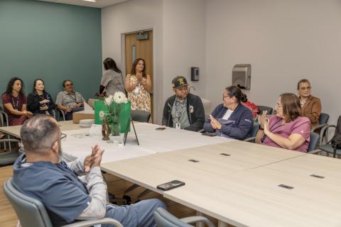Group of people in a conference room with long tables, applauding.