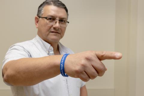 Man in white shirt pointing with blue wristband that says "Stress is tough, so are you"