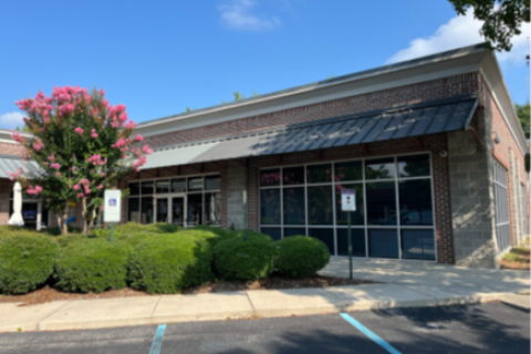 Modern storefront with glass windows, black awning, and greenery in front.