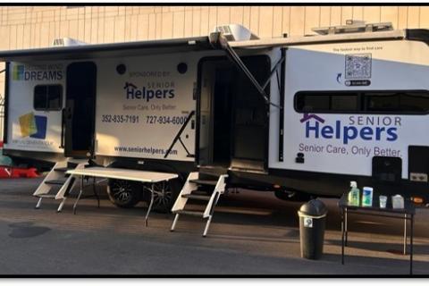 White mobile unit with "Senior Helpers" logo, doors open, and table outside.