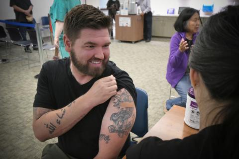 Man with tattoos gets a vaccine from a nurse.