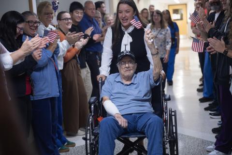 Elderly man in wheelchair applauded by hospital staff.