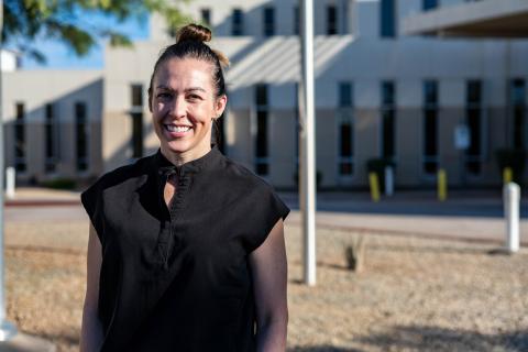 Woman smiling outside a modern building with desert landscape.