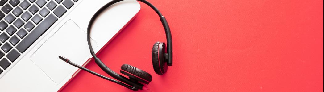 A set of headphones rests on a laptop against a red background