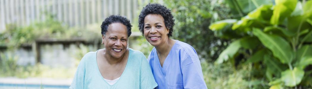 Caregiving nurse in scrubs standing next to elderly woman using a walker