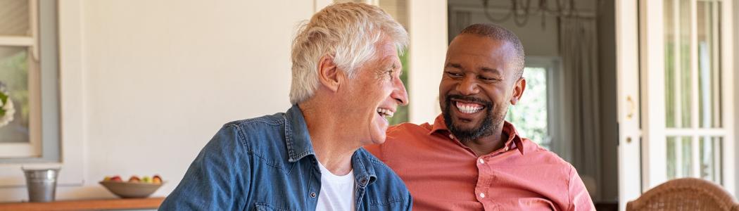 2 middle aged men sitting on a couch smiling