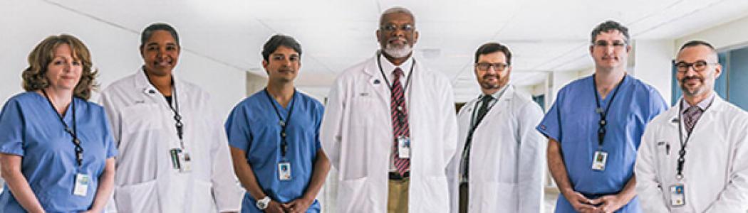 Seven healthcare professionals in scrubs and lab coats standing in a row facing the camera