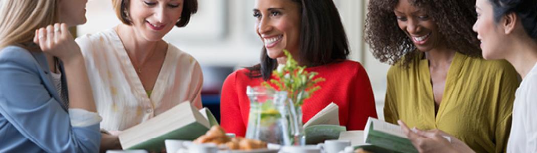 women sitting together smiling while looking at books