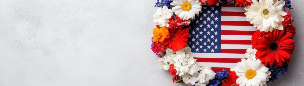 A wreath of red, white, and blue flowers over a United States flag on a gray background.