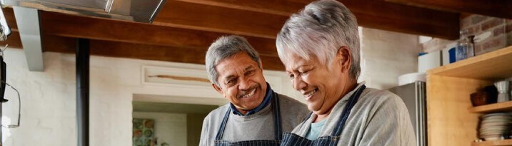 a man with gray hair and moustache wearing a sweater and apron looking and smiling at women with gray hair wearing a gray sweater and apron