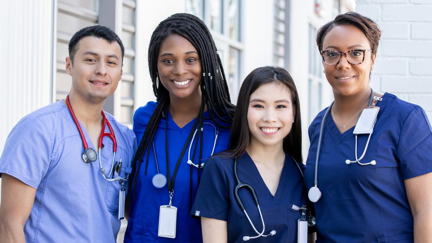 Group of 4 nurses, standing outside, smiling as a group