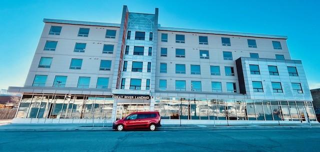 Large multilevel building with Great River Landing sign above main entrance of building. Ground level of building is mostly large glass windows
