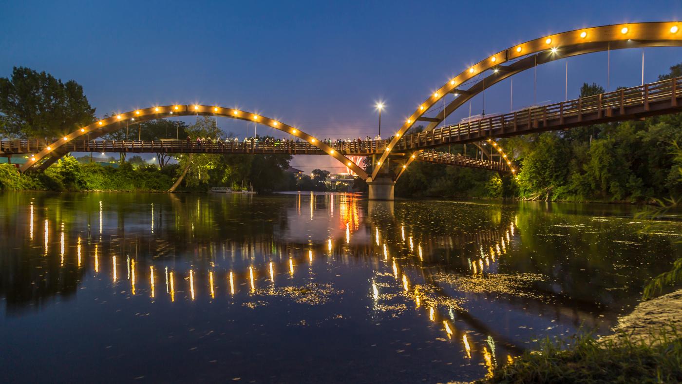 A triangular shaped bridge with lights over a river.