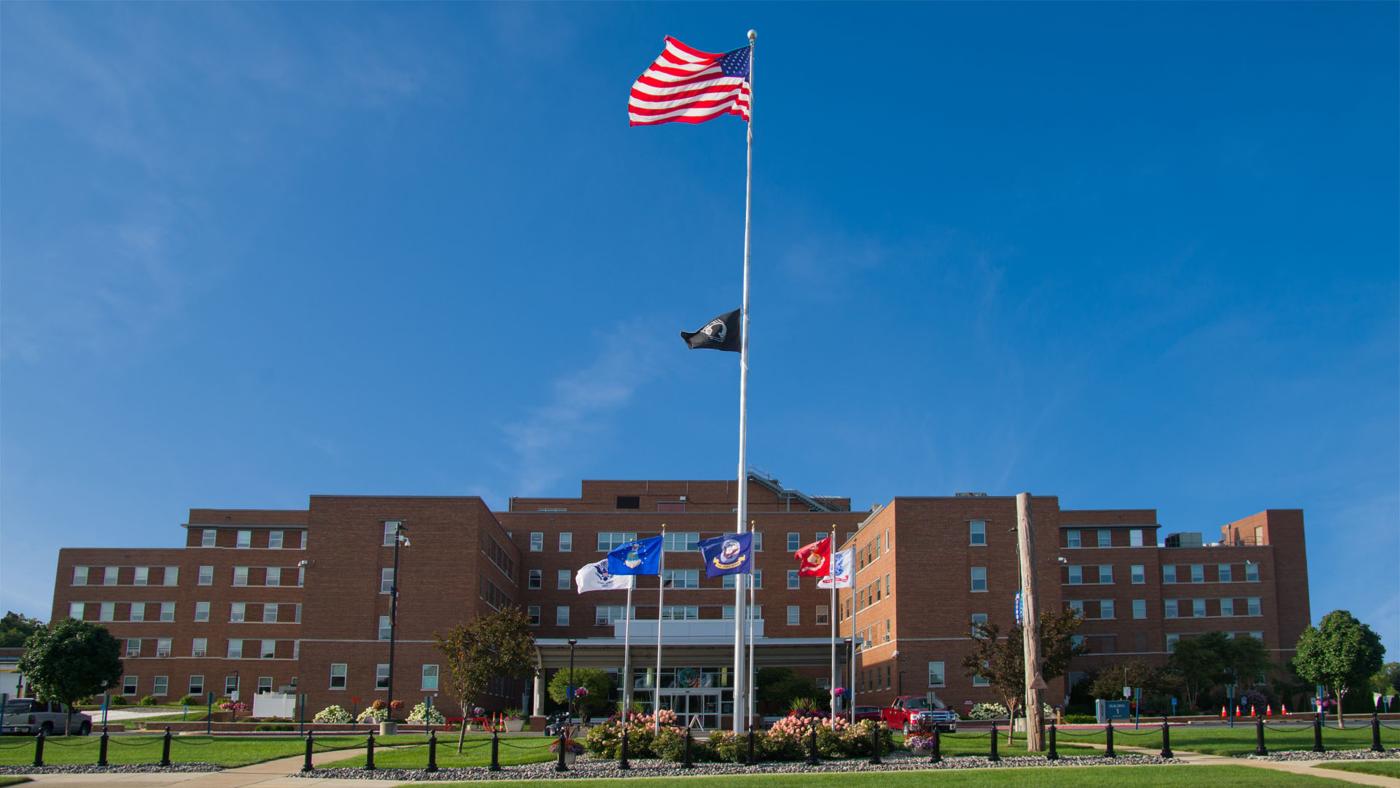 Front of medical center with grass, flags, and blue sky.