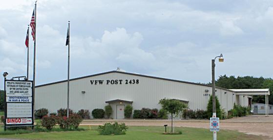Large white building. VFW Post 2438 in black lettering. 3 Flag poles and a sign mentioning bingo.