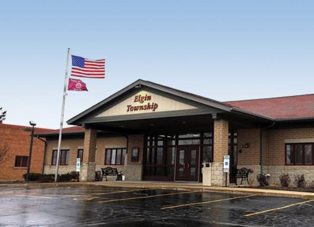 A brown building with two built-in pillars supporting a covered entrance and a nearby flagpole