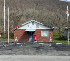 A brick and white wood-clad building with flagpoles on either side of the paved parking area