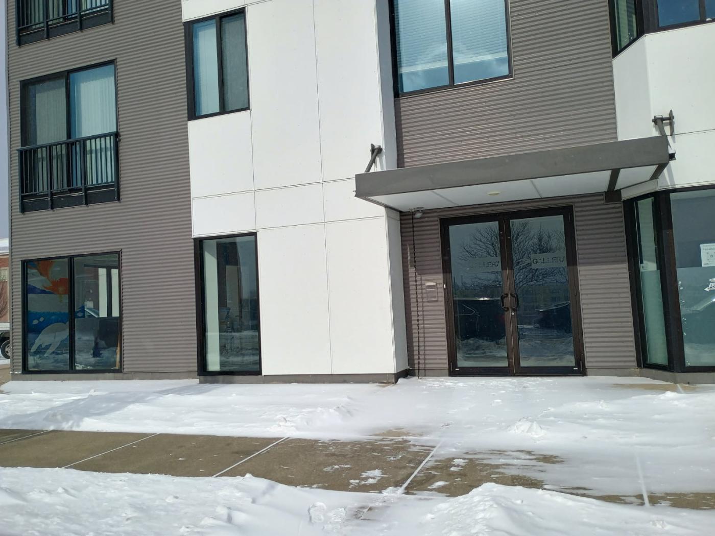 Modern apartment building entrance with snow-covered ground and glass doors.