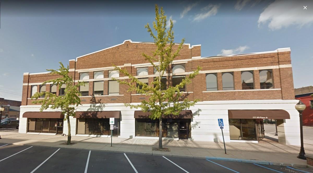 Exterior of brick building with trees and parking lot.