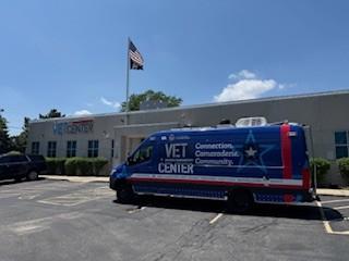 Blue van with "VET CENTER" written on side, parked in front of a building with an American flag.