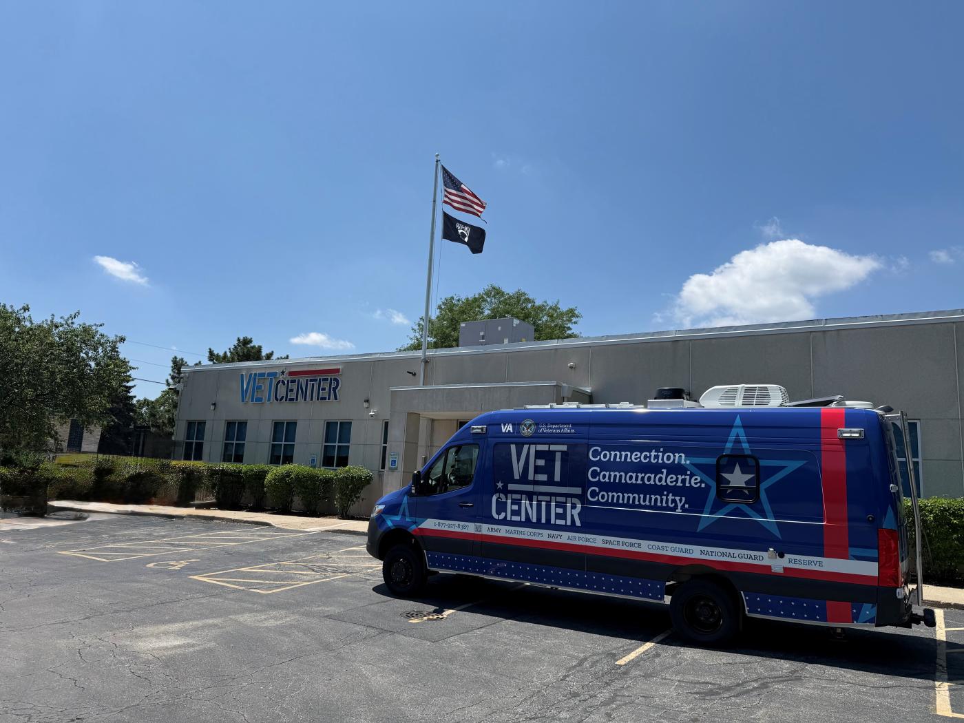 Blue and red van with "VET CENTER" on side parked in front of building with flags.