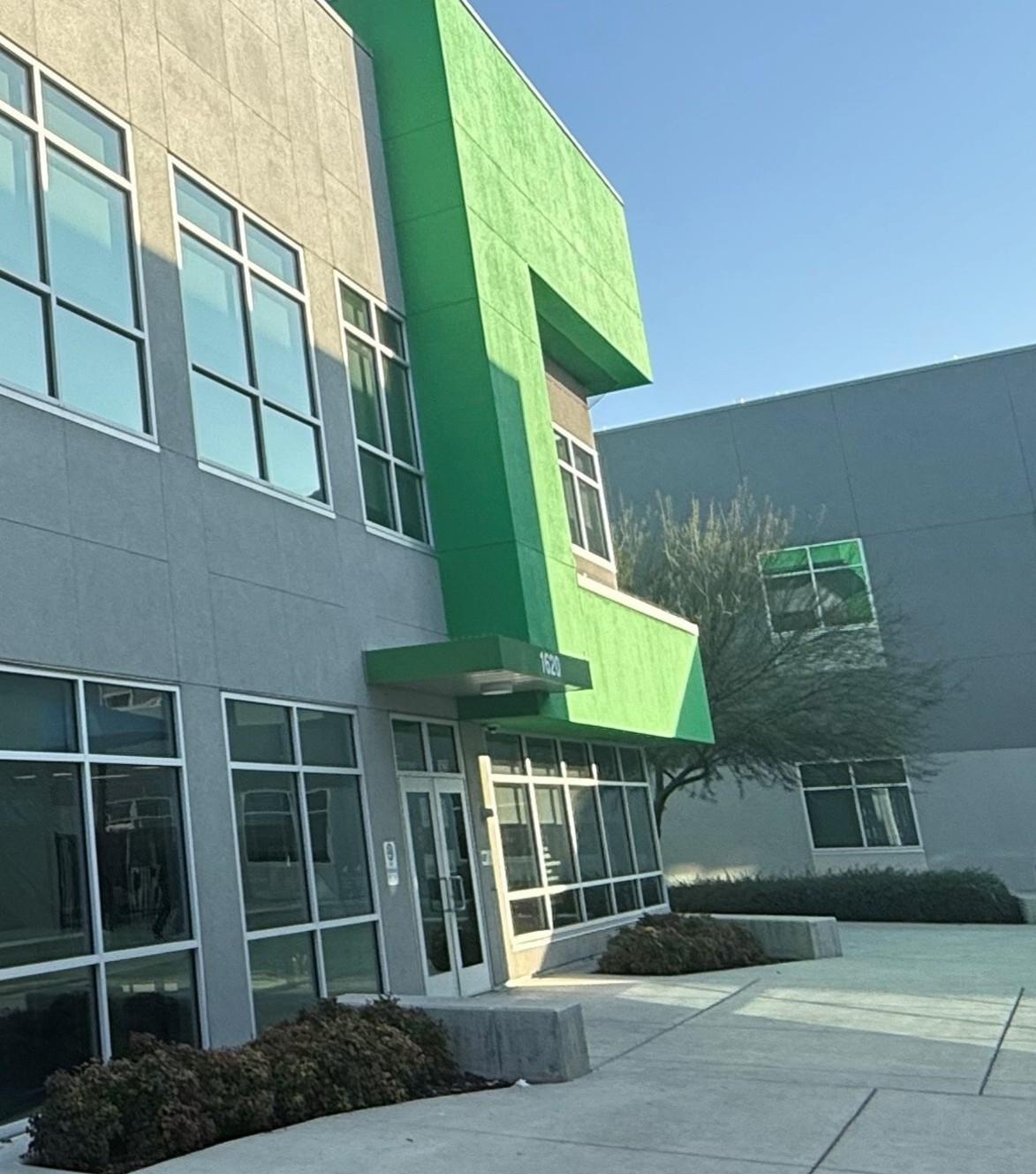 Gray office building with green accents, glass windows, and a tree in front.