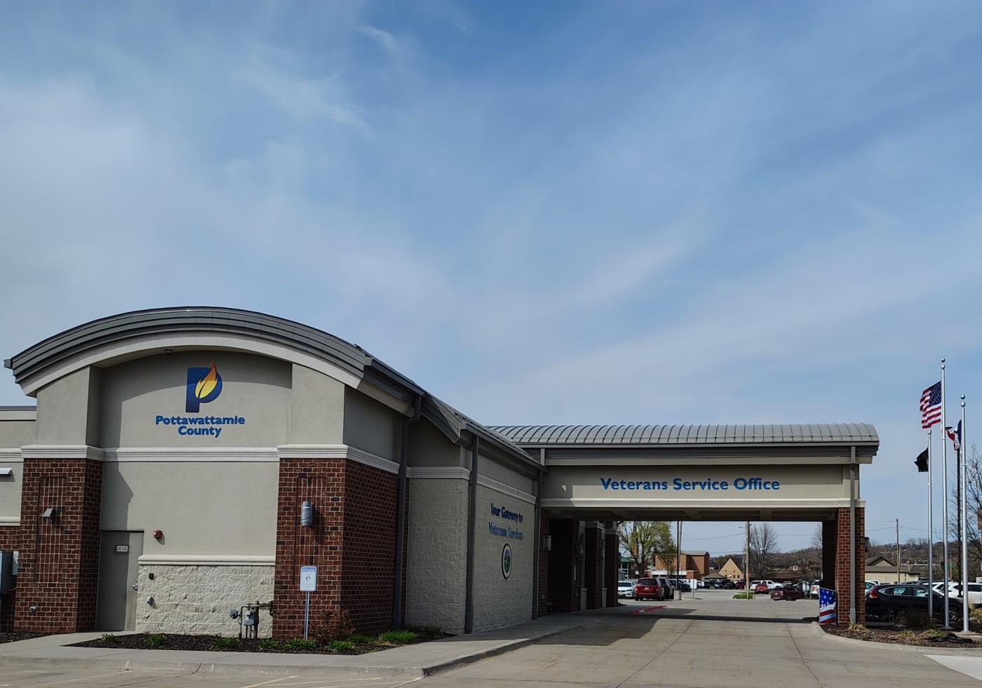 A modern building with a curved entrance, blue sky, and flagpoles.