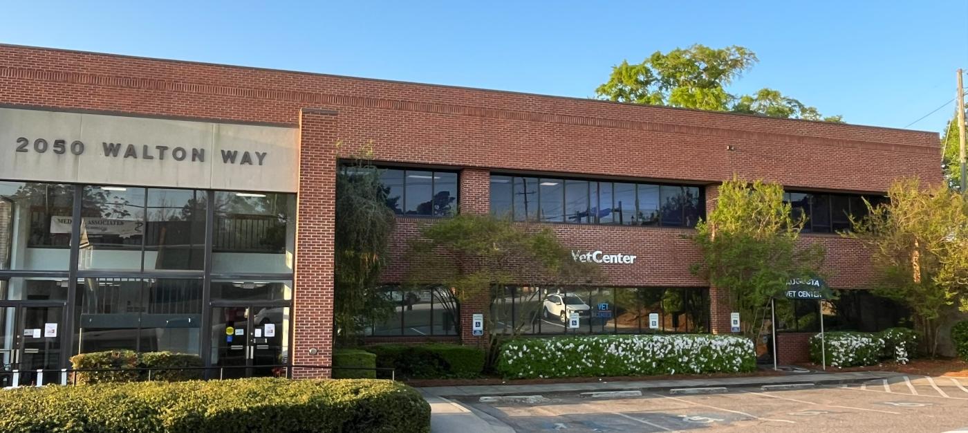 Brick office building with glass windows, bushes, and trees.